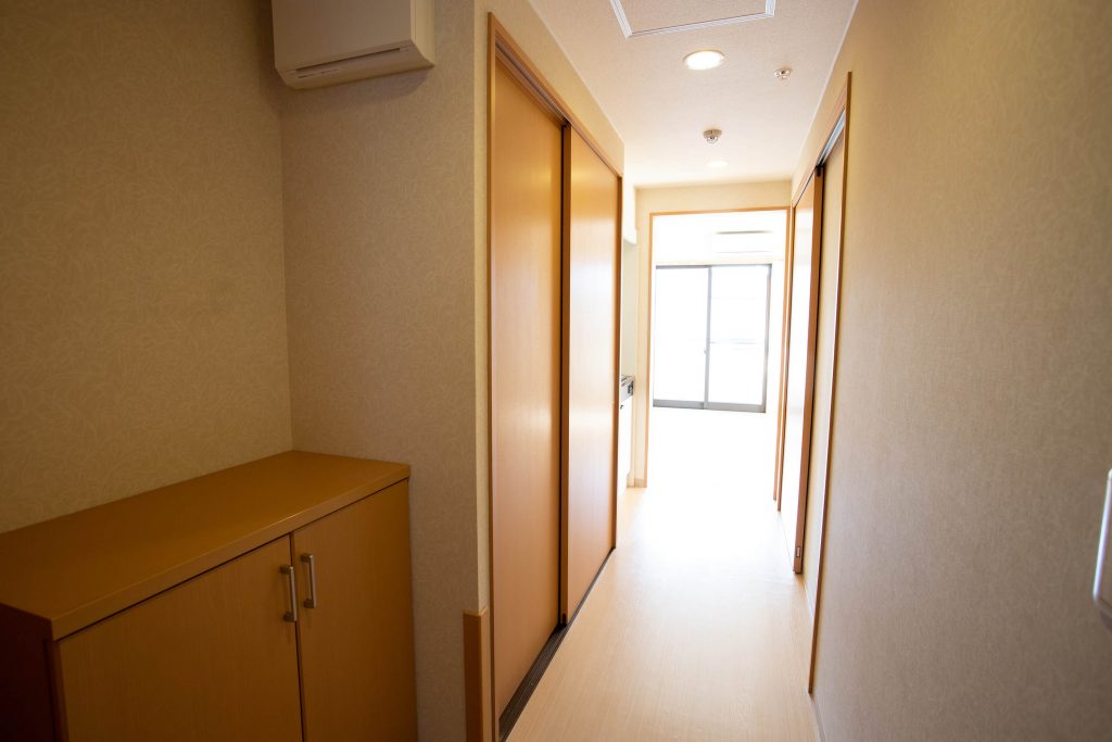 居室の廊下。複数の居室ドアと収納が見える明るい空間。