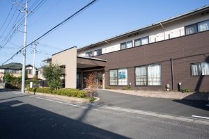 介護施設の外観。茶色と白のモダンな平屋建て、駐車場側からの景観